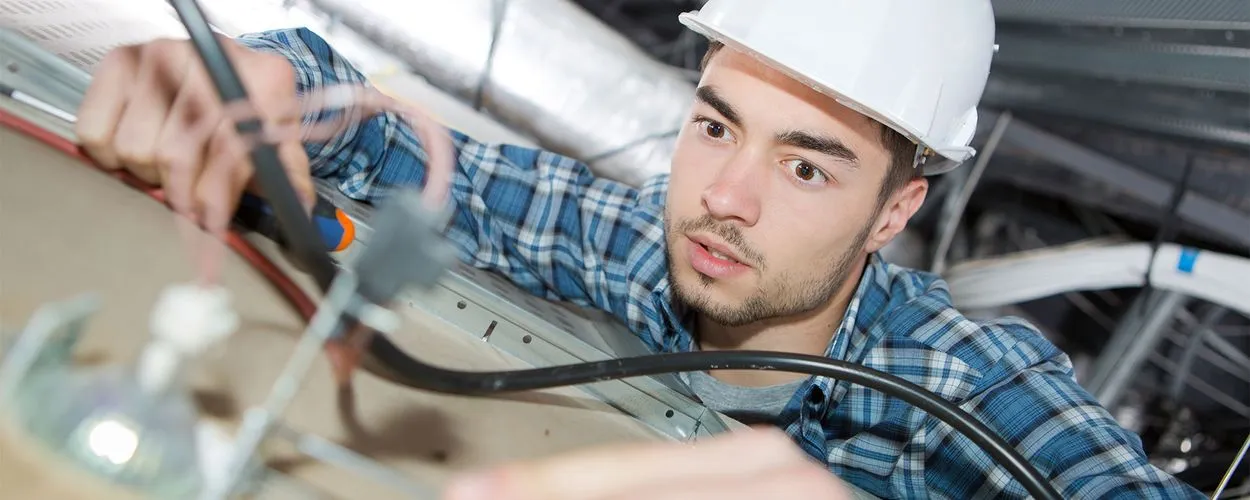 Elektriker mit Schutzhelm installiert sorgfältig Kabel und überprüft elektrische Leitungen.