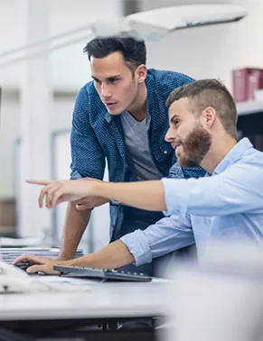 Zwei junge Männer arbeiten zusammen am Computer im modernen Büro und besprechen Daten.